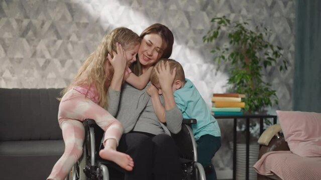 Loving children come to hug mother sitting in wheelchair