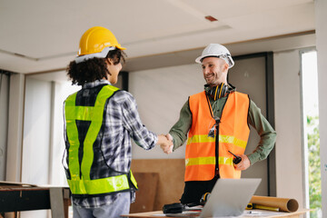 Construction team shake hands greeting start new project plan behind yellow helmet on desk in office center to consults about their building project..