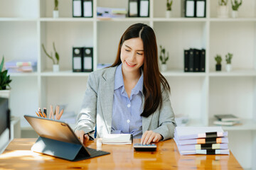 Asian woman freelancer is working her job on computer tablet and laptop Doing accounting analysis report real estate investment data, Financial at office.
