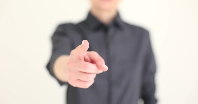 Woman in classic grey shirt points index finger to camera standing on beige background. Blurry female person makes pointing gesture slow motion