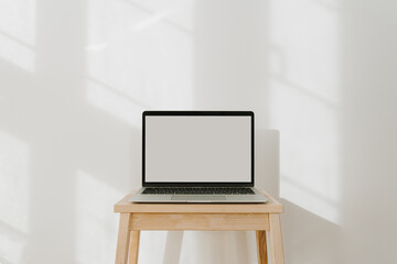 Laptop computer with blank screen and sunlight shadows on the wall. Minimal styled website, online shop, store, social media template with mockup copy space