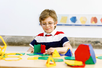 Happy kid boy with glasses having fun with building and creating geometric figures, learning mathematics and geometry