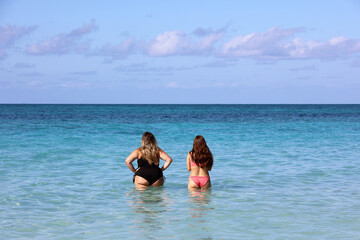 Fat and slim girls in swimwear going to swim in sea water, rear view. Two girlfriends on a beach, overweight and dieting concept