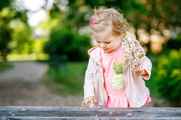 Cute adorable toddler girl playing with blooming chestnut flowers. Little baby child going for a...