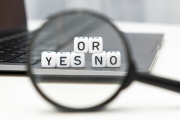 Yes or no on cubes through a magnifying glass and laptop on the background. Chose or shopping...