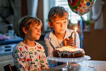 Two beautiful kids, little preschool boys celebrating birthday and blowing candles on homemade...