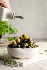 Pouring olive oil over green and black olives in a bowl