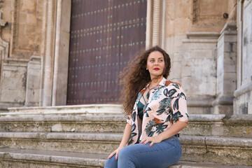 Young beautiful woman, blonde, with curly hair and blue eyes, wearing flower shirt, green top and jeans, sitting on a ladder posing. Concept fashion, beauty, trend, model.