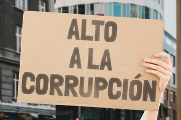 The phrase " Stop Corruption " is on a carton banner in men's hands. Protest. Power. Government. Criminal. Illegal. Fraud. Impunity. Collusion. Graft. Bribery. Lobbying. Kickback. Nepotism. Patronage