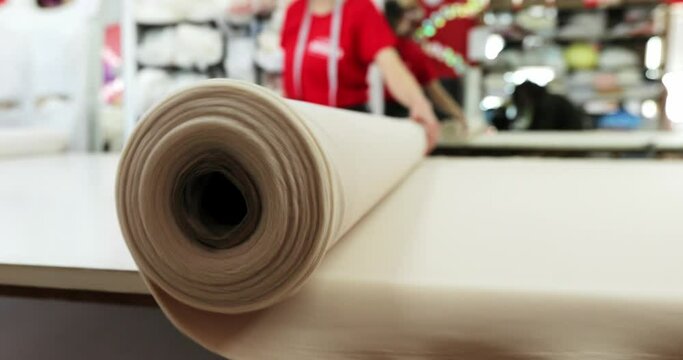 a seamstress in a red dress rolls out a roll of beige fabric on a table at a dress factory. close-up red background