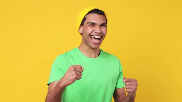 Fun happy young man of African American ethnicity wear green t-shirt hat countdown 1 2 3 one two three go celebrate win scream doing winner hands gesture say yes isolated on plain yellow background