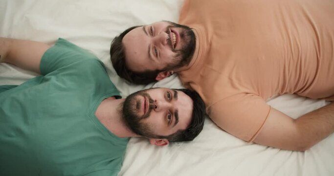 Portrait of attractive bearded gay men couples laying on bed together, talking. Top view footage