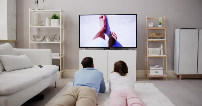 Young Happy Couple Lying On Carpet Watching Movie On Television
