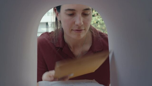 Young woman getting correspondence and parcel box out of the mailbox, reading information on labels, then closing the door. POV shot from inside of the mailbox
