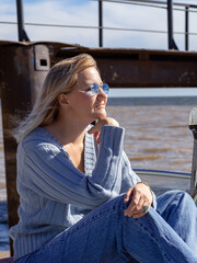 Portrait of a young beautiful girl in a blue sweater and jeans is on a boat near the river pier

