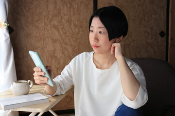 スマホを見て考え事をする黒髪ショートヘアの女性	