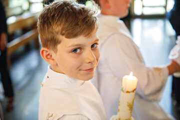 Little kid boy receiving his first holy communion. Happy child holding Christening candle....