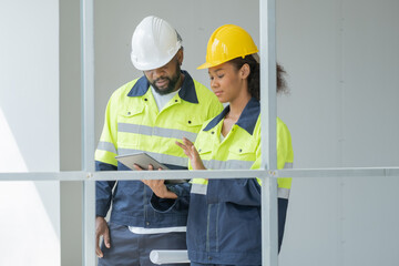 Black engineer walking at work site on building, Portrait of engineer checking work on tablet together, teamwork working concept with full engineering cloth.