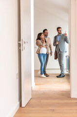 Young married couple talking with a real-estate agent visiting an apartment for sale or for rent. Future parents buying an apartment. Real estate concept. A new beginning - 586090821