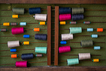 Colourful sewing threads hanging on old wooden sticks against a green texture wall. Decoration background. 