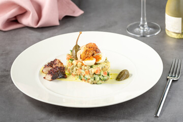 Russian salad with aioli sauce, shrimp, octopus and capers on a white porcelain plate