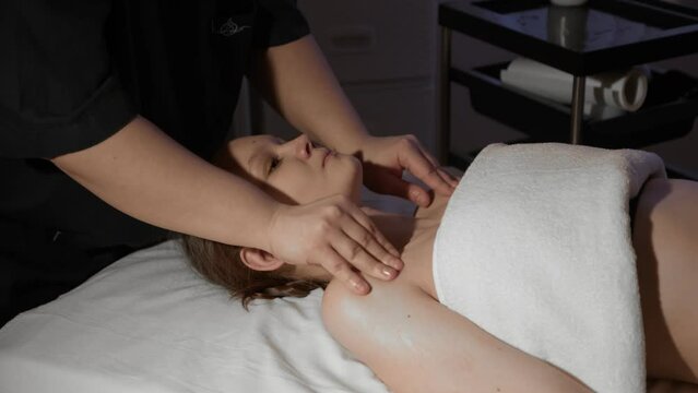 A masseuse makes a back massage to a young woman in a spa center, close-up.