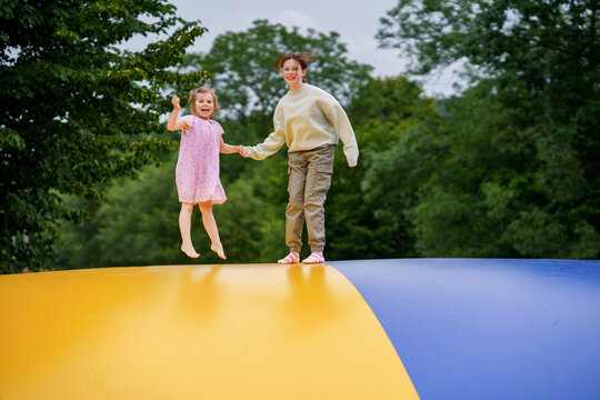 Little preschool girl and school sister jumping on trampoline. Happy funny children, siblings in love having fun with outdoor activity in summer. Trampolin in ukrainian flagg colors