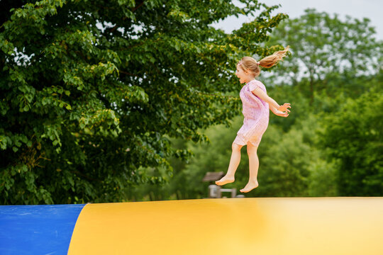 Little preschool girl jumping on trampoline. Happy funny toddler child having fun with outdoor activity in summer. Sports and exercises for children. Trampolin in ukrainian flagg colors