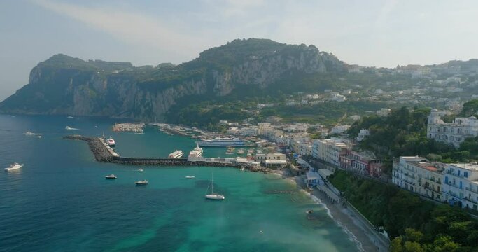 Aerial Panning Shot Of Nautical Vessels Moored In Sea By Hotels On Mountain During Sunny Day - Capri, Italy