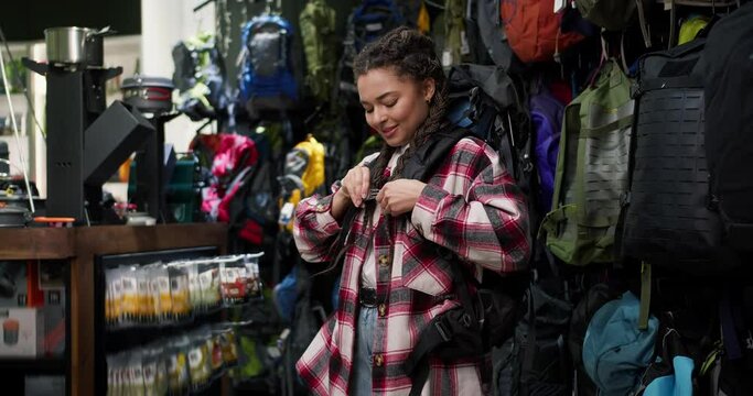 Young woman trying big tourist rucksack in sports equipment store