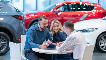 Happy caucasian couple signs a contract for the purchase of a car salon.