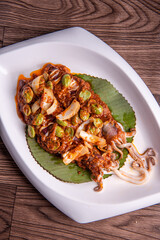 grilled bbq fresh whole seafood squid sooting octopus with spicy samba chilli sauce and petai smelly bean vegetables on banana leaf plate wood table asian halal food menu
