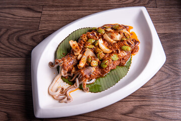 grilled bbq fresh whole seafood squid sooting octopus with spicy samba chilli sauce and petai smelly bean vegetables on banana leaf plate wood table asian halal food menu