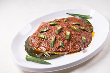 grilled bbq fresh whole seafood stingray fish with spicy samba chilli sauce and lady finger vegetables on banana leaf plate wood table asian halal food menu