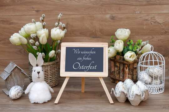 Osterkarte Frohe Ostern. Ein Strauß Tulpen, Osterhasen und Eier mit dem Text Wir wünschen ein frohes Osterfest auf einer Tafel.