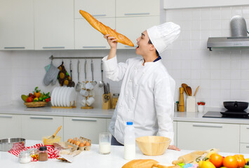 asian professional male pastry chef in white cooking uniform and tall cook hat standing smiling posing at counter full of baking equipment and ingredients.
