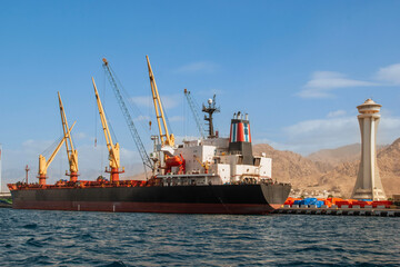 Jordan. Aqaba. Container ship moored at the dock for loading. There are several cranes on pier....