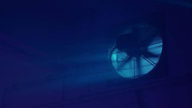 Interior night shot of an empty basement. Blue light, dirty window and fan. 