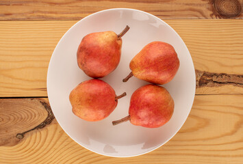 Several organic Bartlett pears in a white ceramic plate on a wooden table, macro, top view.