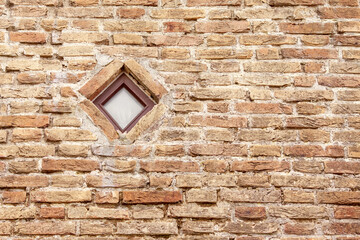 Fototapeta na wymiar Brick wall with a small square window. Brown brick wall of a house in the old town with a rhombus window