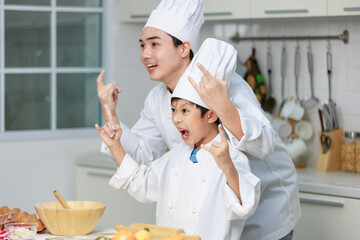 Asian young little boy chef and male cooking teacher in uniform with white tall cook hat standing...