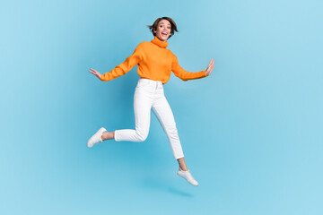 Fototapeta na wymiar Full size photo of pretty young girl jumping excited cheerful energetic dressed stylish orange clothes isolated on blue color background