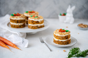 Easter Carrot cake with cream cheese frosting and marzipan decorations on a white stone background for festive dinner. Small easter bento cake. Fresh homemade carrot dessert. Traditional Easter food.