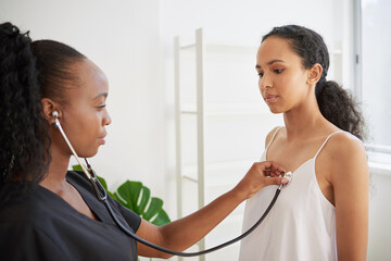 Black female doctor listens to patient's heartbeat at medical checkup