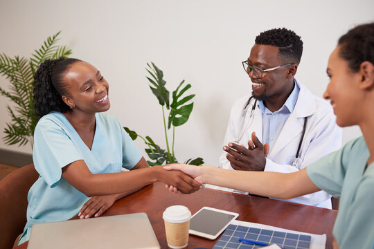 Two doctors shake hands while colleague claps, medical promotion achievement