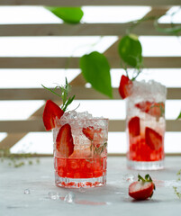 Fresh homemade lemonade with ice, soda and strawberry. Cold summer mocktail on a sunny light background.