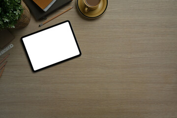 Digital tablet, notepad, coffee cup and potted plant on wooden table. White screen for for your advertising text message