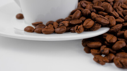 A cup of coffee and coffee beans on a white background. Roasted coffee beans on a white saucer, close up.