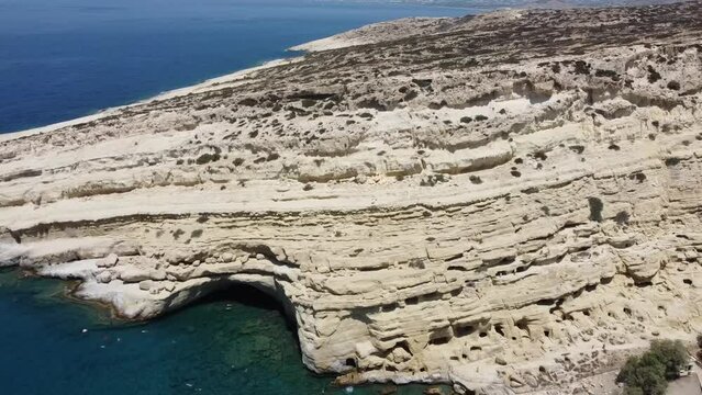 Aerial drone view of famous Matala beach with caves, known for hippies in the 70's. View of the beach from rock caves, once a roman cemetery, in famous greek beach Matala, Crete, Greece.