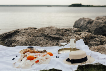 Fototapeta na wymiar Concept of summer picnic on the hill with amazing view on the sea. Wine and two wineglasses on the golden tray, eco shopping bag with oranges, straw hat and croissants, berries and cheese brie.
